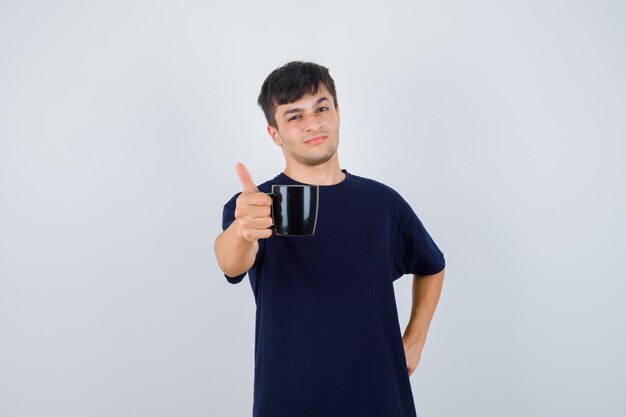 검은 티셔츠에 커피 한 잔을 제공하고 자랑스럽게 보이는 젊은 남자. 전면보기.