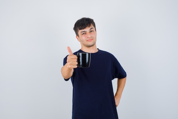 Young man offering a cup of coffee in black t-shirt and looking proud. front view.