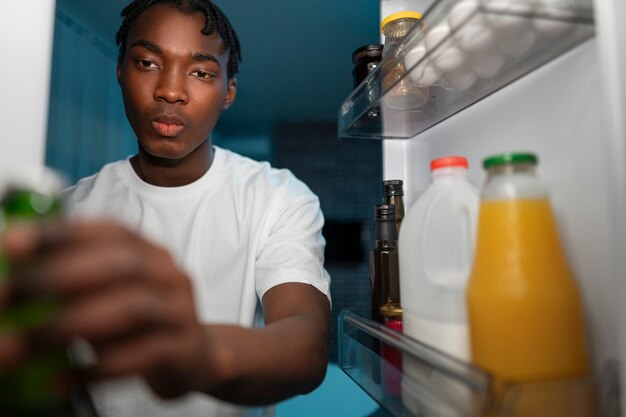 Молодой человек открывает холодильник дома, чтобы перекусить посреди ночи