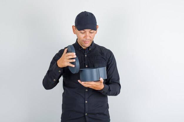 Young man opening gift box in black shirt with cap and looking surprised