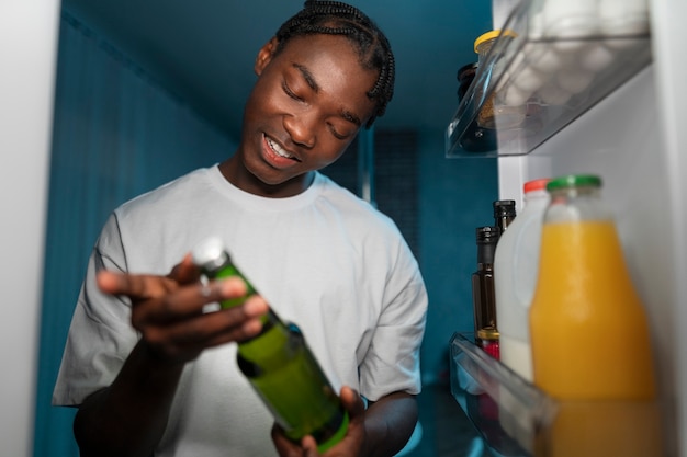 Бесплатное фото Молодой человек открывает холодильник дома, чтобы перекусить посреди ночи