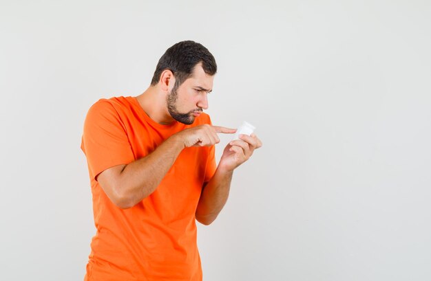 Young man in orange t-shirt reading info on bottle of pills , front view.