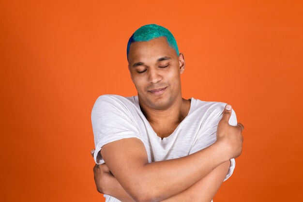Young man on orange wall hugging himself