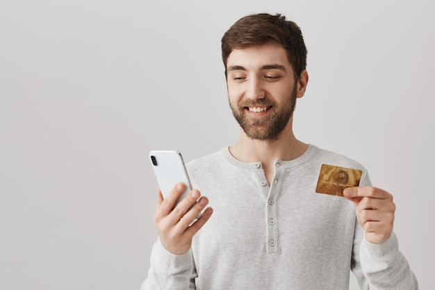 若い男が携帯電話を使用して、クレジットカードでオンラインで注文します。