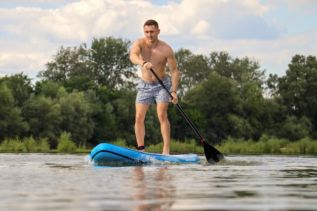 Молодой человек катается на доске с веслом на реке в дневное время