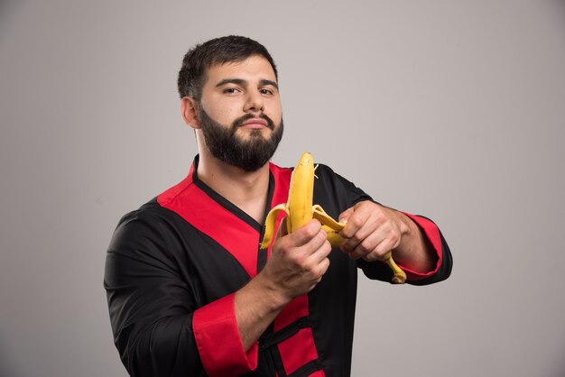 Young man peeling a banana on dark surface.