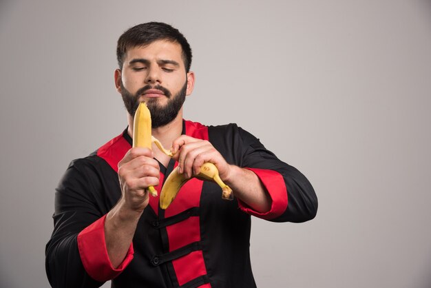 Young man peeling a banana on dark wall.