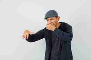 Free photo young man pinching nose due to bad smell in t-shirt, jacket, cap and looking disgusted , front view.