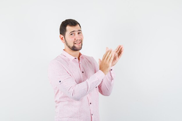 Молодой человек в розовой рубашке аплодирует после выступления на конференции и выглядит довольным