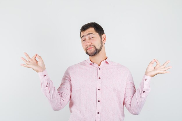 Young man in pink shirt doing meditation with closed eyes and looking relaxed