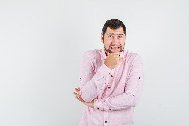 Young man in pink shirt holding chin while looking up and looking troubled