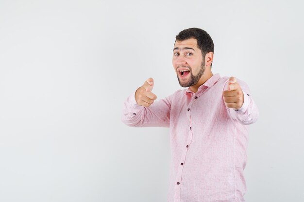 Young man in pink shirt pointing at camera and looking optimistic