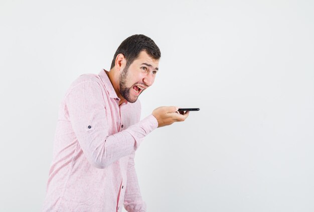 Young man in pink shirt shouting while recording voice message and looking furious