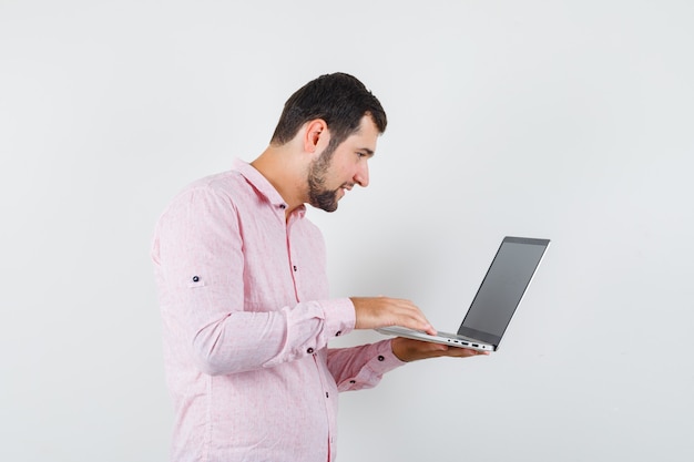 노트북 컴퓨터를 사용하고 바쁜 찾고 분홍색 셔츠에 젊은 남자