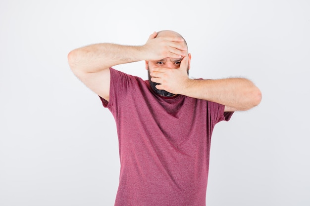 Young man in pink t-shirt looking through hands and looking serious , front view.