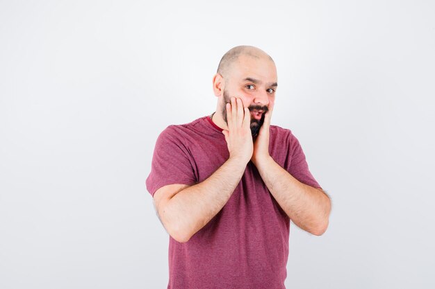 Young man in pink t-shirt putting hands near mouth and looking optimistic , front view.