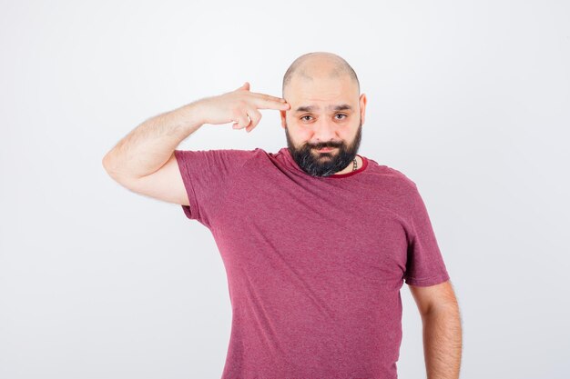 Young man in pink t-shirt showing gun gesture and looking dismal , front view.