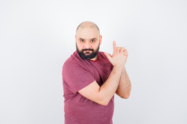 Young man in pink t-shirt showing pistol gesture , front view.