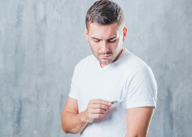 Young man placing the medical digital thermometer in his under armpit