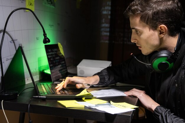 해커 공격을 계획하는 젊은 남자. 노트북을 사용하여 헤드폰을 끼고 코드를 입력하는 남자. 해킹, 기술, 사이버 범죄 개념