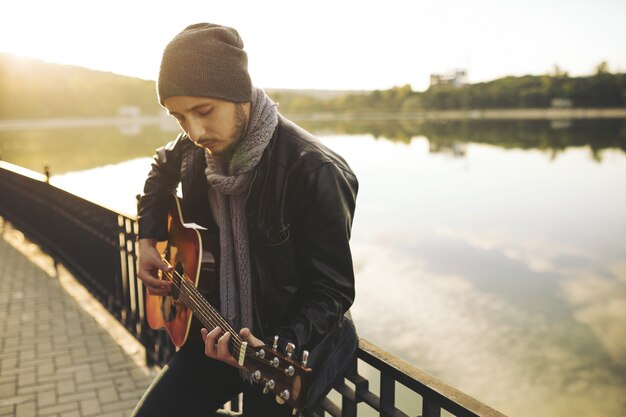 Young man playing on guitar at the lake