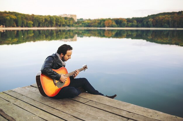 Молодой человек играет на гитаре на озере