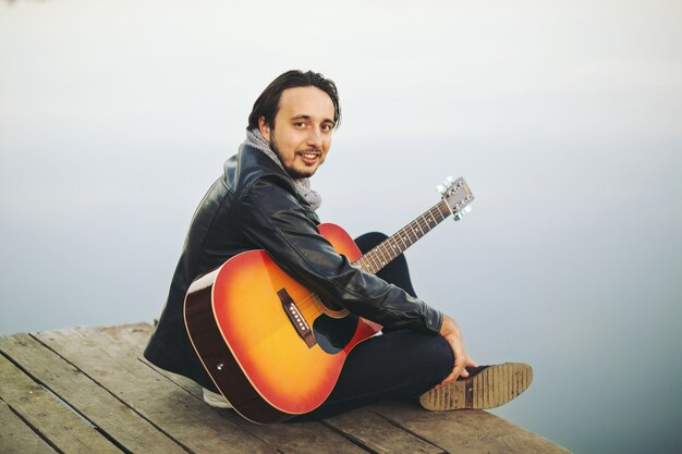 Young man playing on guitar at the lake