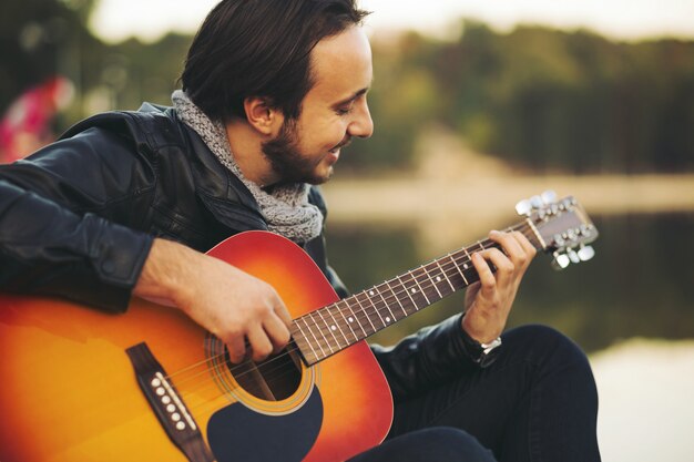 Young man playing on guitar at the lake