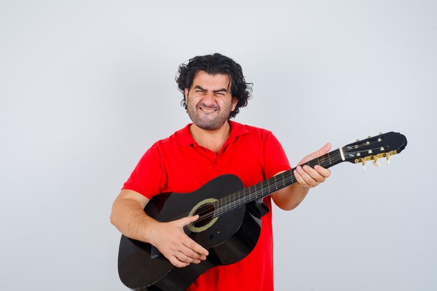 Young man playing on guitar in orange t-shirt and looking confident