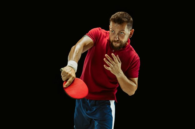 Young man playing table tennis on black studio