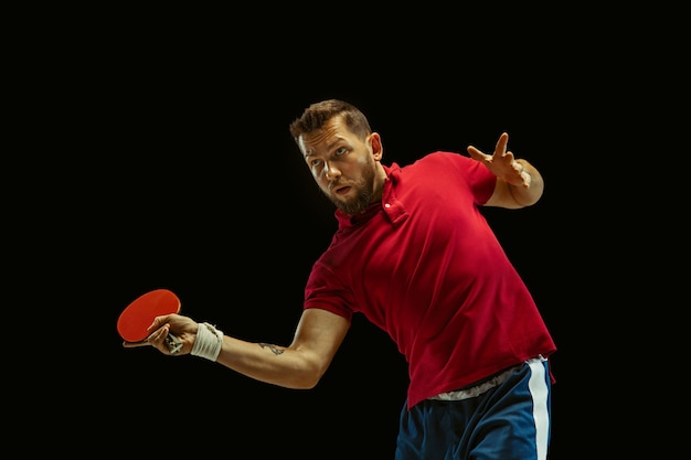 Young man playing table tennis on black studio