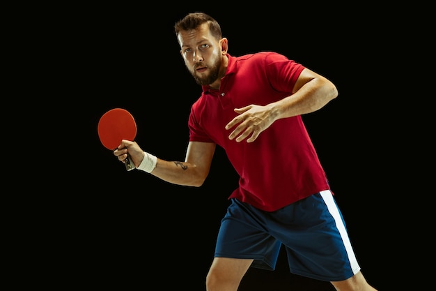 Young man playing table tennis on black studio