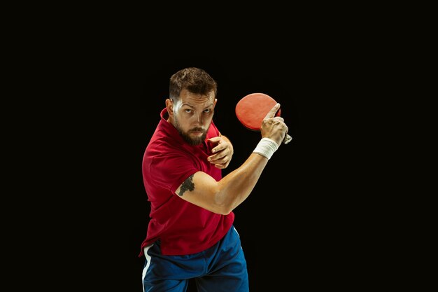 Young man playing table tennis on black studio