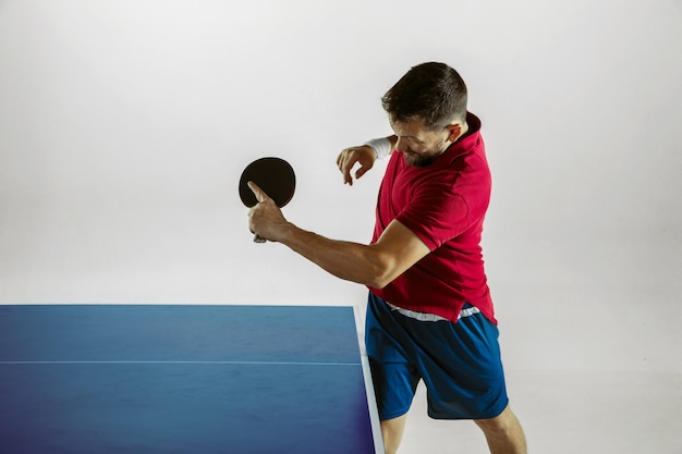 Young man playing table tennis on white studio wall