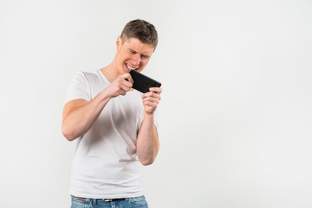 Young man playing video game on mobile phone against white backdrop