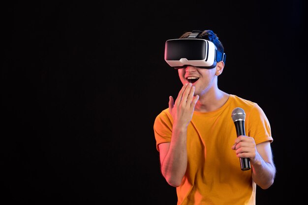 Young man playing virtual reality and singing on dark surface