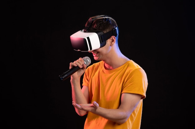 Young man playing virtual reality and singing on dark surface