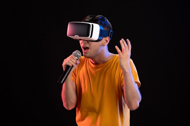 Young man playing virtual reality and singing on dark surface