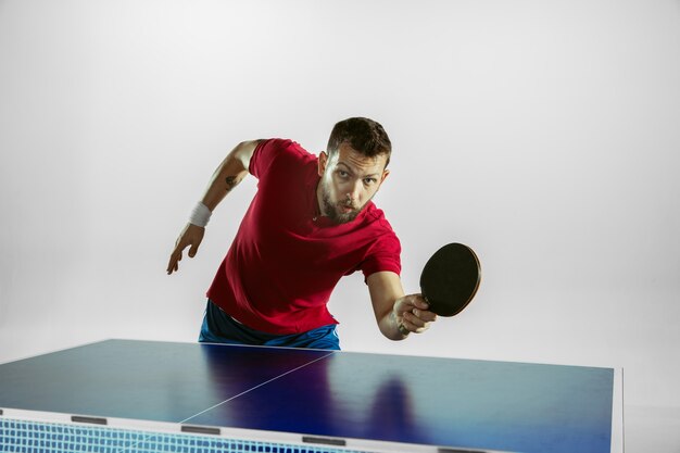 Young man plays ping pong on white wall.