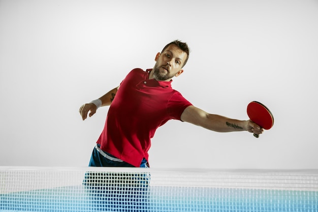 Young man plays ping pong on white wall.