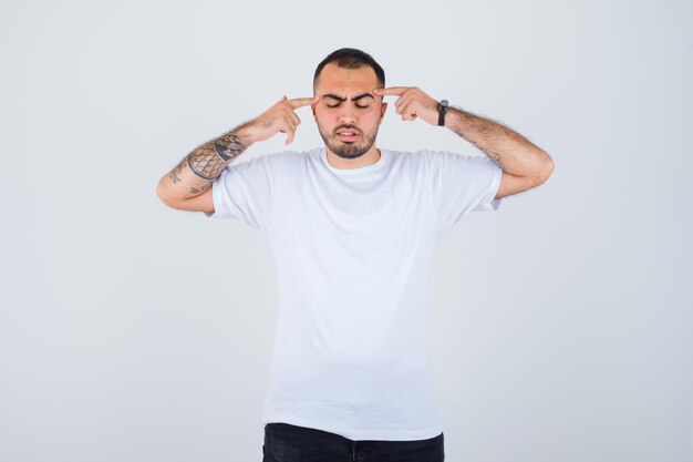 Young man plugging ears with index wingers in white t-shirt and black pants and looking serious