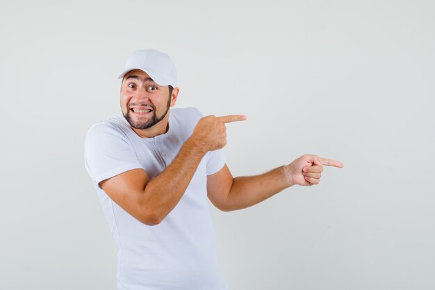 Young man pointing aside in t-shirt and looking joyful , front view.