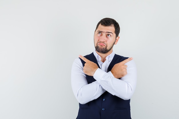 Young man pointing away in shirt, vest and looking hesitant