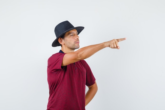 Young man pointing away in t-shirt, hat , front view.