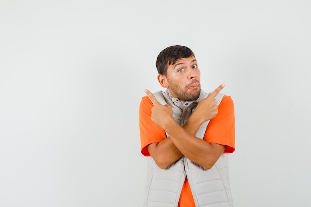 Young man pointing away in t-shirt, jacket and looking confused , front view.