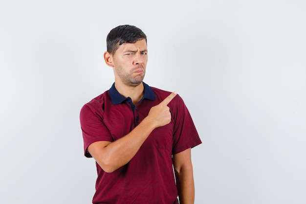 Young man pointing away in t-shirt and looking dissatisfied. front view.