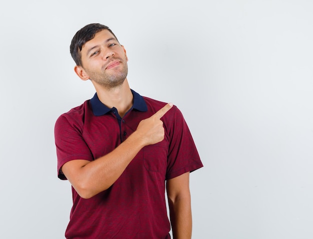 Young man pointing away in t-shirt and looking merry , front view.