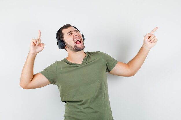 Young man pointing away while enjoying music in green t-shirt and looking energetic