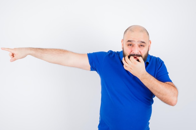 Young man pointing away while whistling in blue shirt , front view.