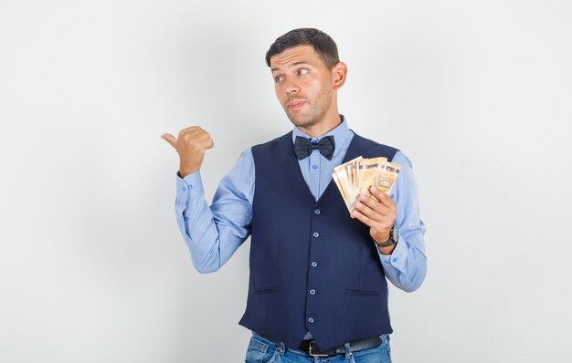 Young man pointing away with money in suit, jeans 